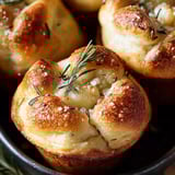 A bowl of muffin-shaped herby bread with a golden top.